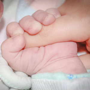 Un bébé tenant le doigt d'une personne.