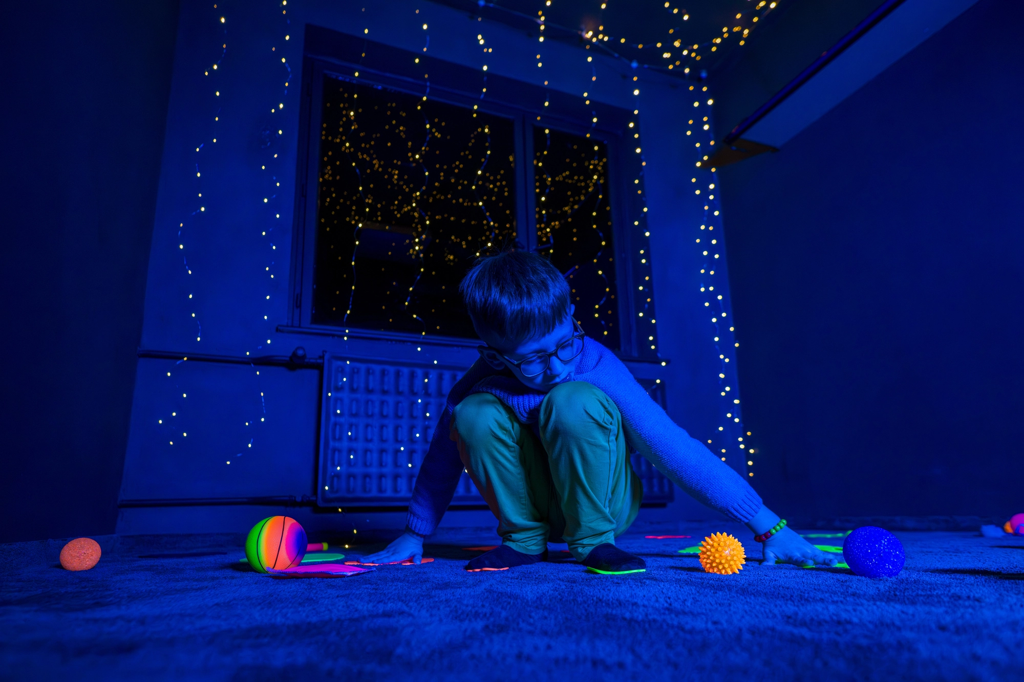 Un enfant découvre l'approche Snoezelen dans une salle à la lumière tamisée, bleutée, avec du matériel de couleur